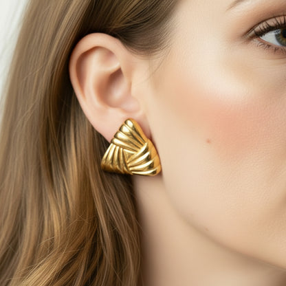 Gold earrings worn by a person with a neutral background